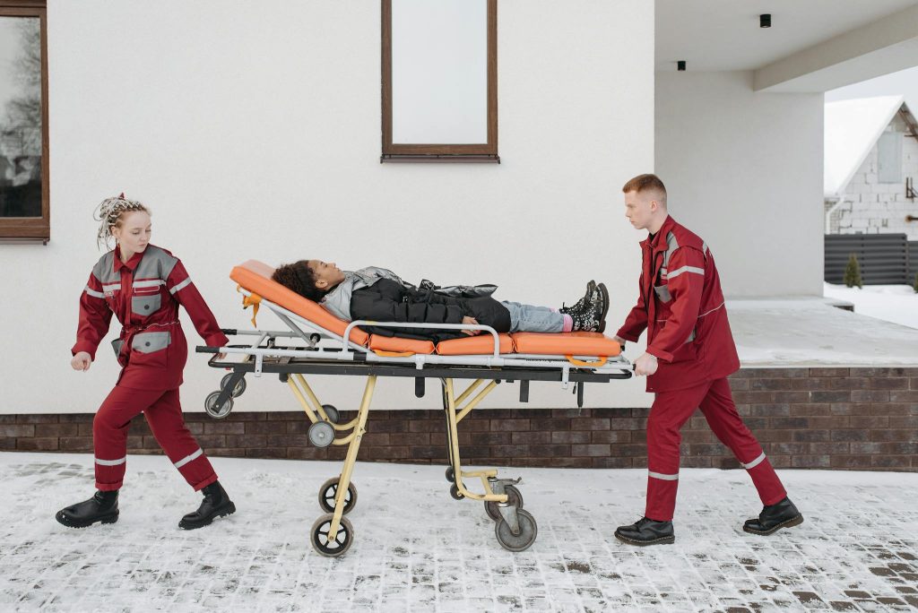 Paramedics assist a patient on a stretcher outside a building during winter.